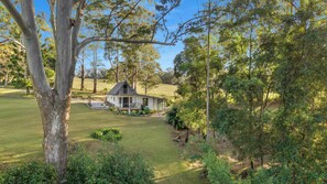 A house with a lawn and trees in the background. - The Cottage at Indooroopilly (Bellawongarah)