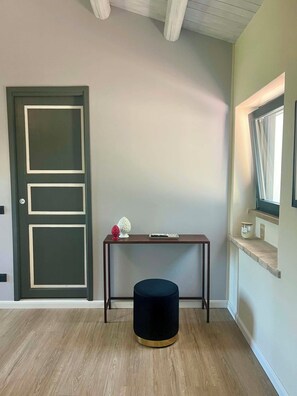 Ein Zimmer mit einer dunklen Holztür, einem kleinen Tisch mit einer Vase und einem runden Hocker.