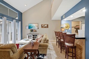 A modern living room with a sofa, coffee table, and dining area with chairs. There is a TV mounted on the wall and a decorative wall piece. - Stunning Lake Conroe 3BR Escape w/ Pool Access (Montgomery)