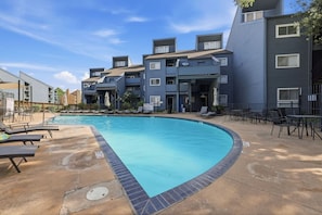 Ein Schwimmbecken mit Liegestühlen und einer Terrasse, umgeben von mehrstöckigen Gebäuden mit Balkonen.