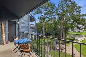 A balcony with a table and chairs, a welcome sign, and a view of a pond and buildings. - Stunning Lake Conroe 3BR Escape w/ Pool Access (Montgomery)