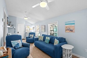 Ein Wohnzimmer mit einem blauen Sofagarnitur, einem weißen Beistelltisch und einem Deckenventilator.