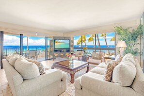 A spacious living area with a large window overlooking a beach, furnished with sofas and a coffee table. - The Kaanapali Alii by Maui Resort Rentals (Kaanapali)