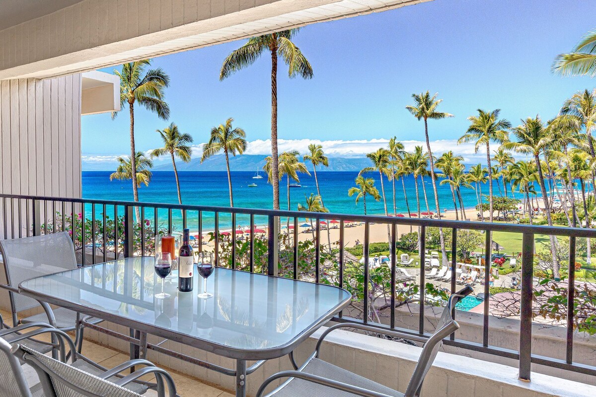 A balcony with a glass table, metal chairs, and a view of the beach and ocean.