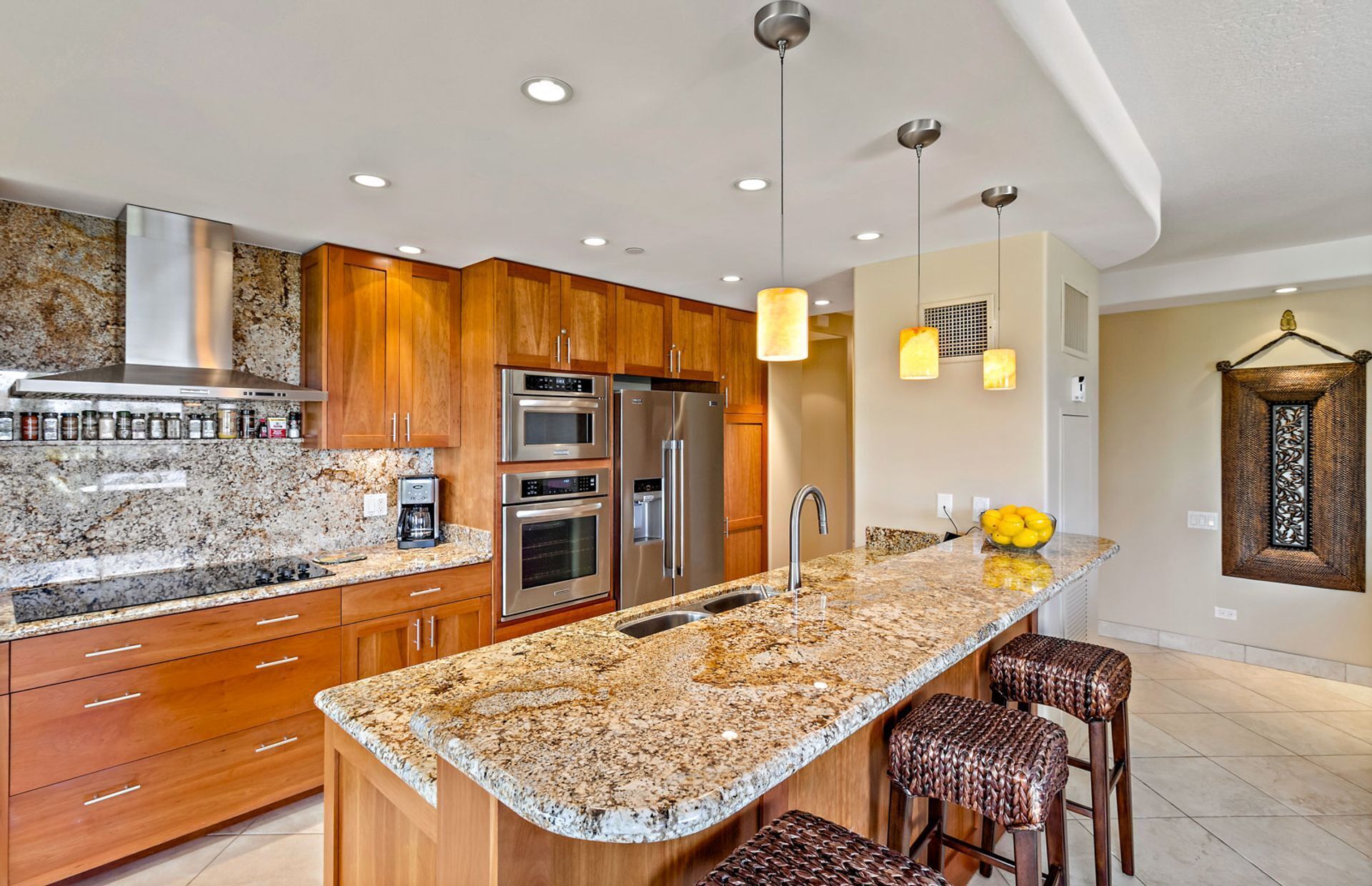 A kitchen with granite countertops, stainless steel appliances, wooden cabinets, and pendant lighting.