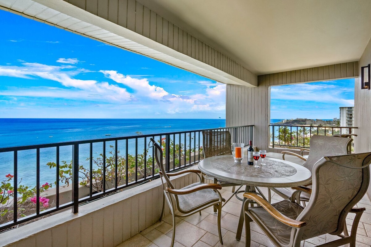 A balcony with a table and chairs, overlooking a coastal view.