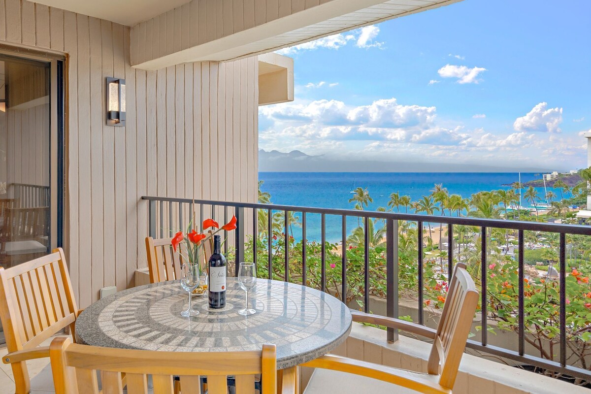 A round table with chairs and a bottle of wine on a balcony overlooking a beach.