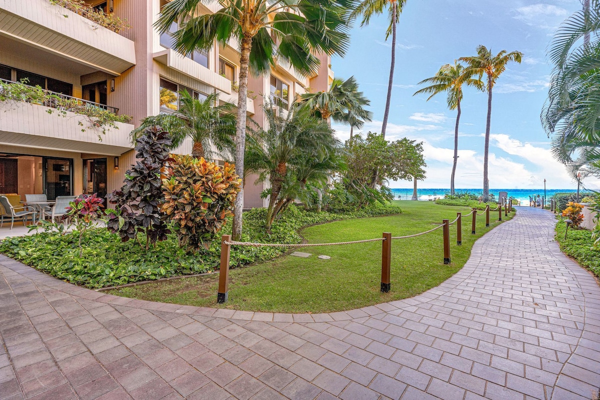 A hotel courtyard with a paved walkway, palm trees, and a view of the ocean.