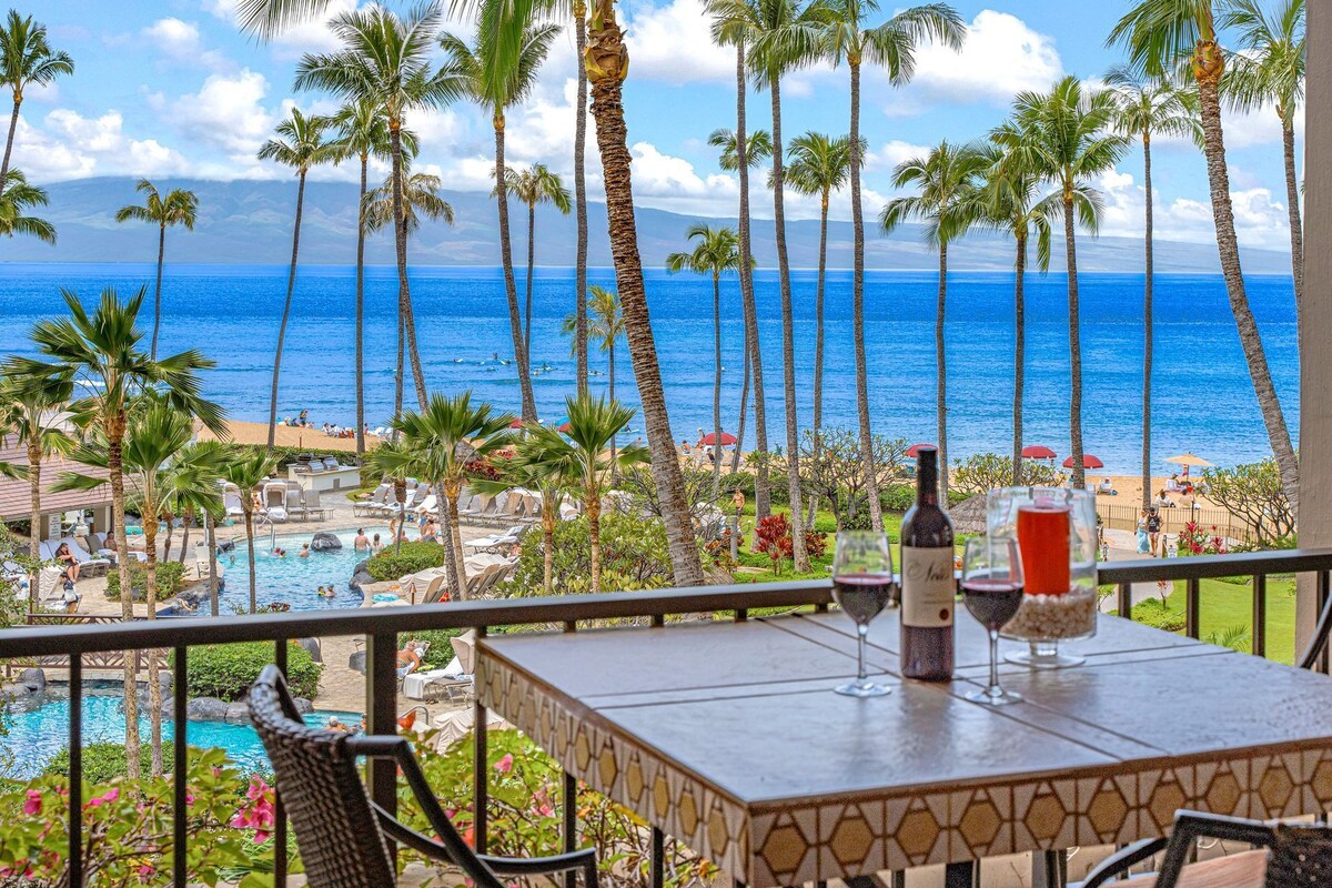 A balcony with a view of a pool, palm trees, and the ocean.