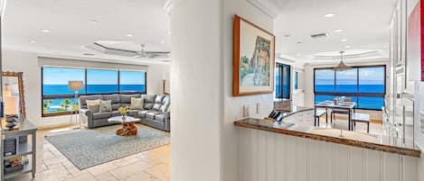 A spacious living area with a large window overlooking the ocean, a dining area with a view, and a kitchen with a large window.