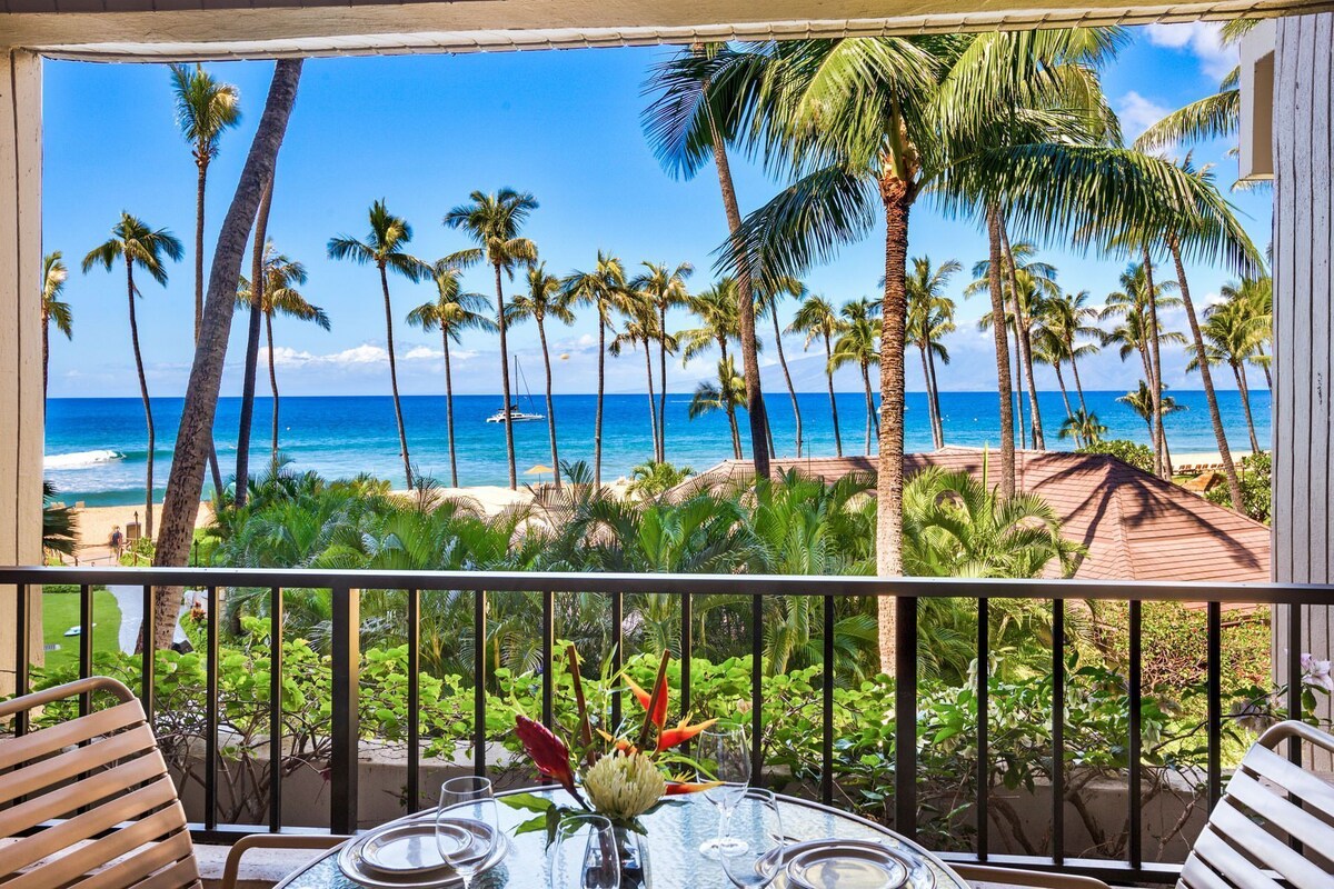 A balcony with a view of a beach and ocean, featuring palm trees and a clear sky.
