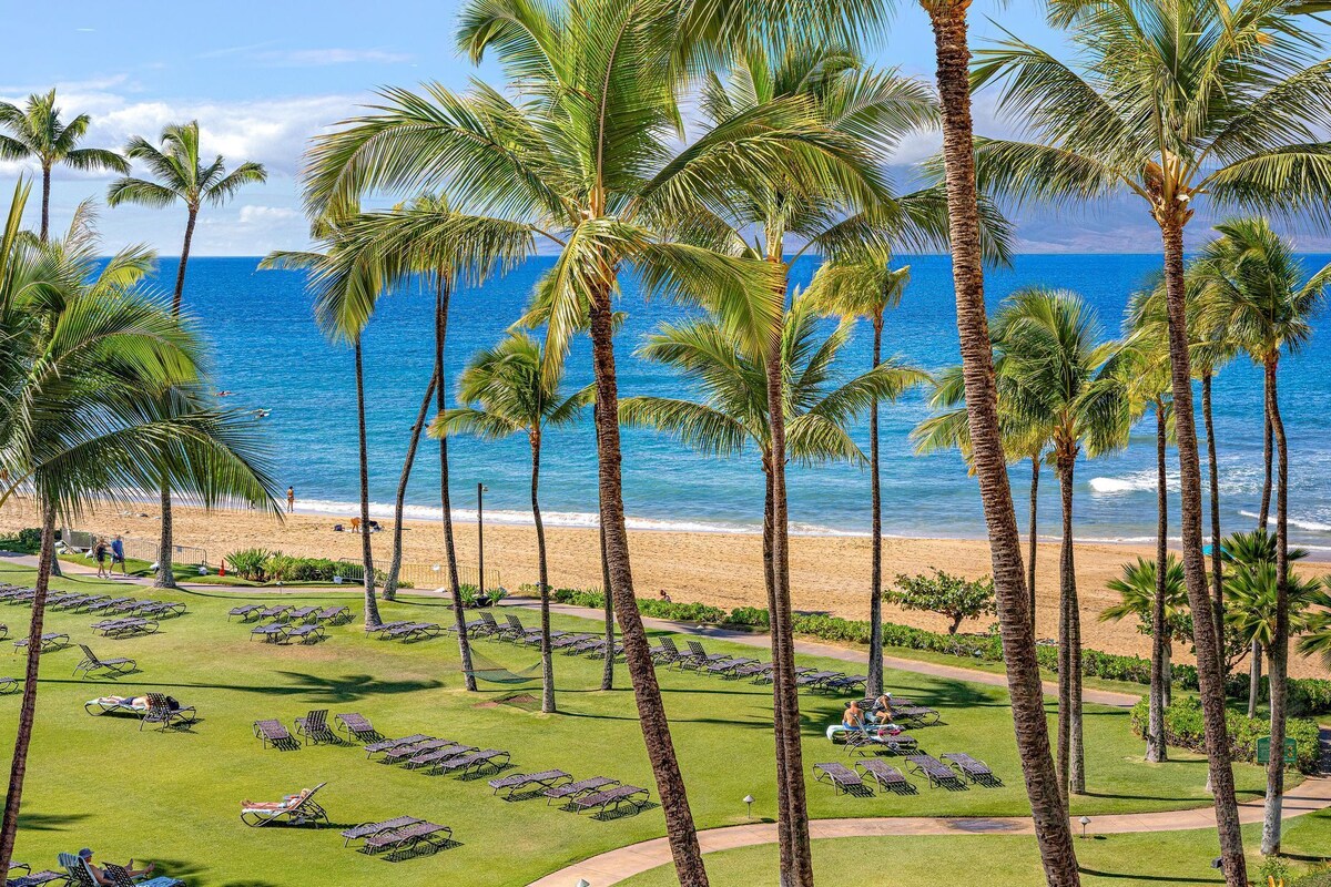 A resort with a beach view, palm trees, and sun loungers.
