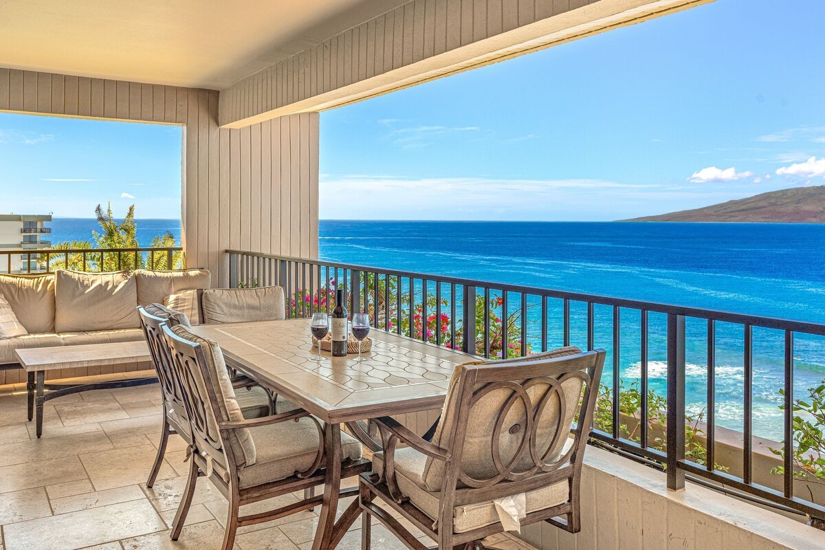 A balcony with a table and chairs, overlooking a coastal view.