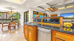 A modern kitchen with wooden cabinets, a built-in dishwasher, and a large island with a sink. - The Kaanapali Alii by Maui Resort Rentals (Kaanapali)