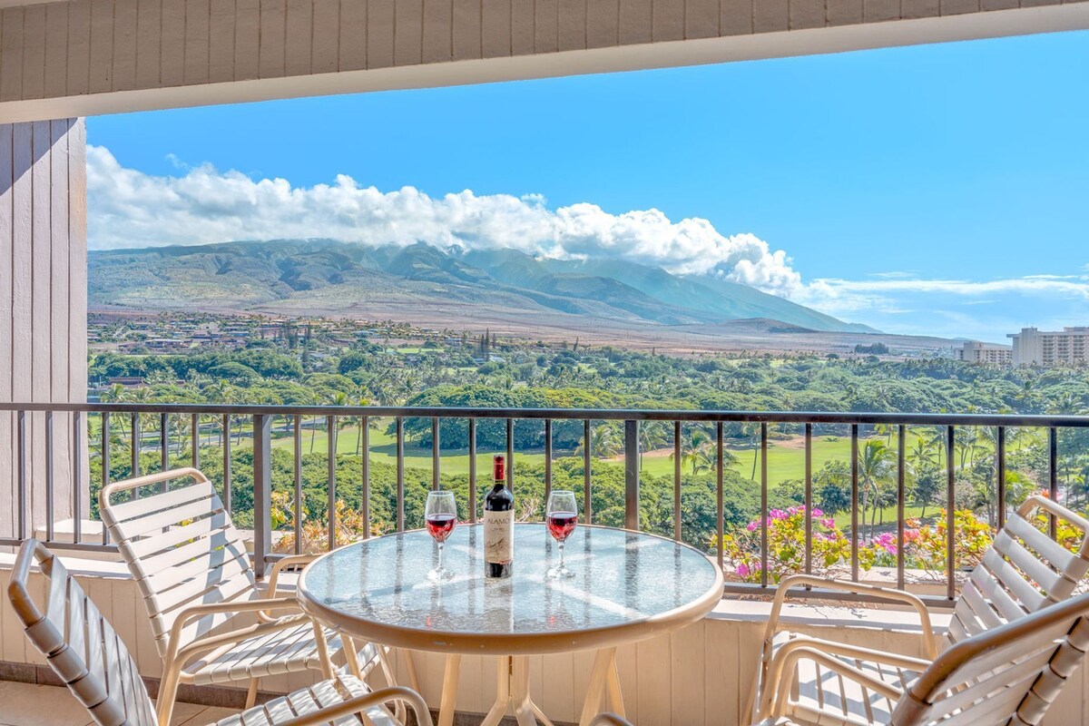 A balcony with a round glass table, two chairs, and two wine glasses with bottles.