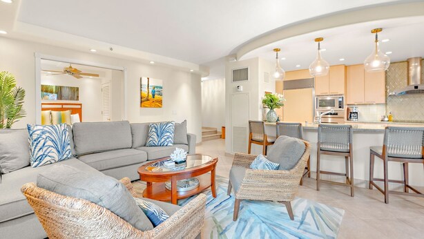 A modern living room with a sofa, chairs, a coffee table, and a kitchen area with bar stools. - The Kaanapali Alii by Maui Resort Rentals (Kaanapali)