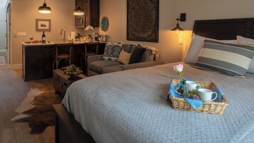 Un dormitorio acogedor con una cama grande, un escritorio y una silla. Hay una bandeja con una rosa y una taza sobre la cama.