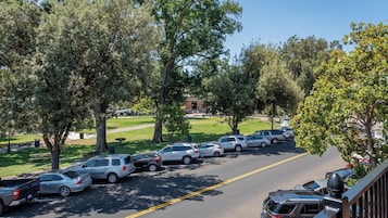 Un estacionamiento con coches y árboles, una zona verde y un edificio al fondo.