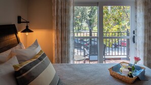 A hotel room with a bed, a nightstand, a lamp, a window with curtains, and a balcony with a view of the street and cars. - Paso Park Suites by Avantstay Park-view Balcony Downtown Paso Robles (Paso Robles)