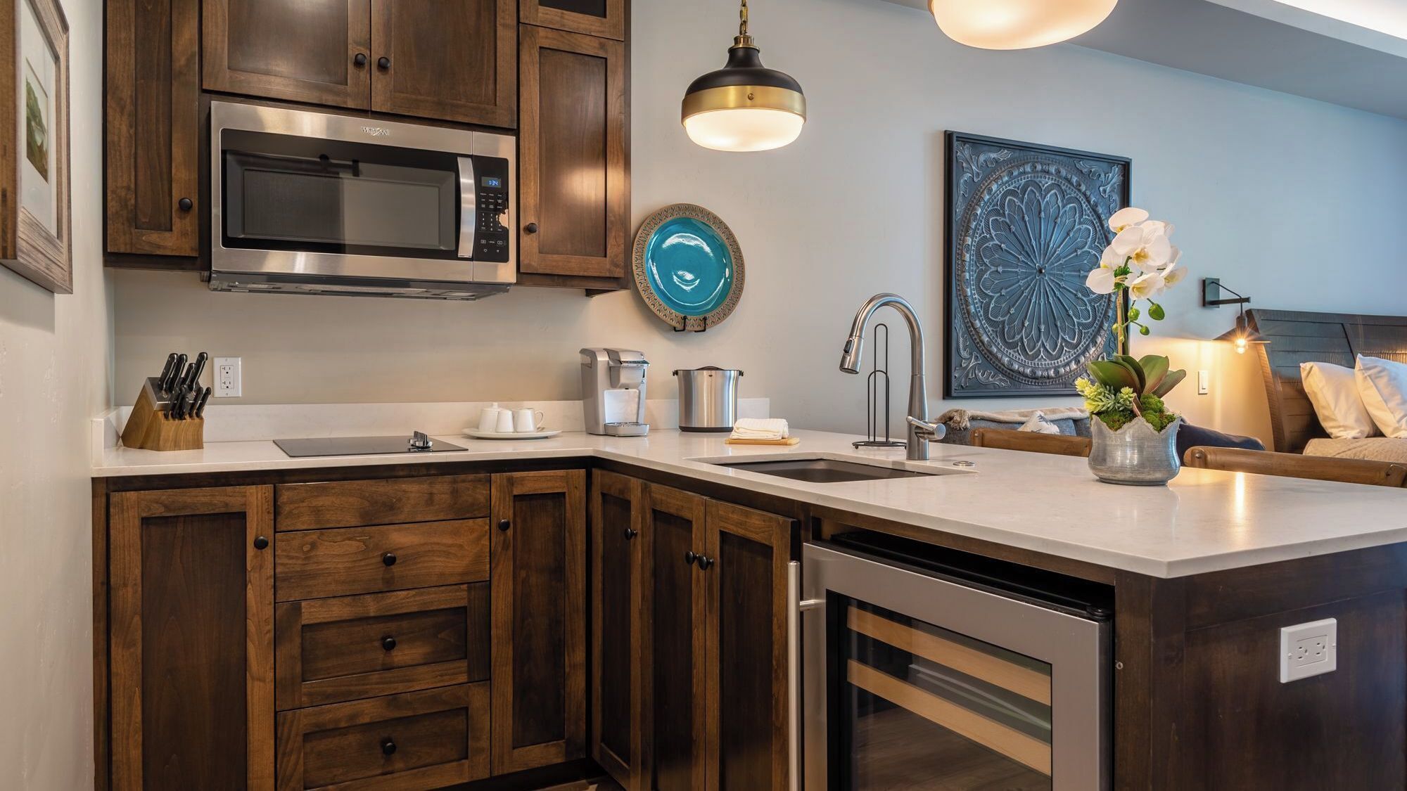 A modern kitchen with wooden cabinets, a stainless steel microwave, a coffee maker, and a sink.