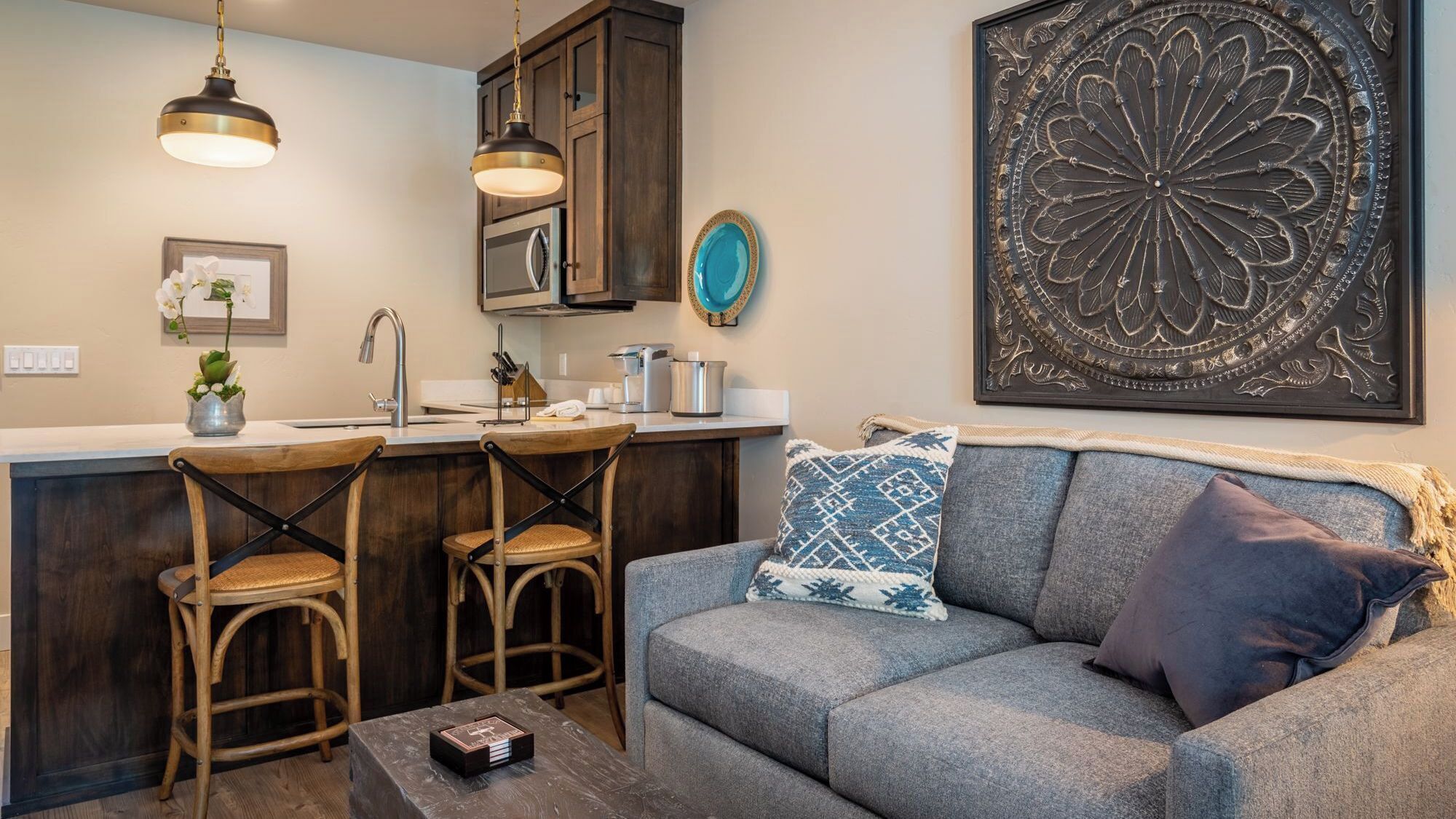 A kitchen with a bar area, two bar stools, a coffee table, and a sofa with decorative pillows.