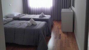 Ein Zimmer mit zwei Betten, einem kleinen Schreibtisch und einem Fenster mit Vorhängen.
