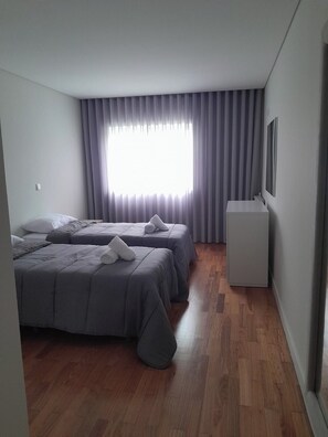 Ein Zimmer mit zwei Betten, einem kleinen Schreibtisch und einem Fenster mit Vorhängen.