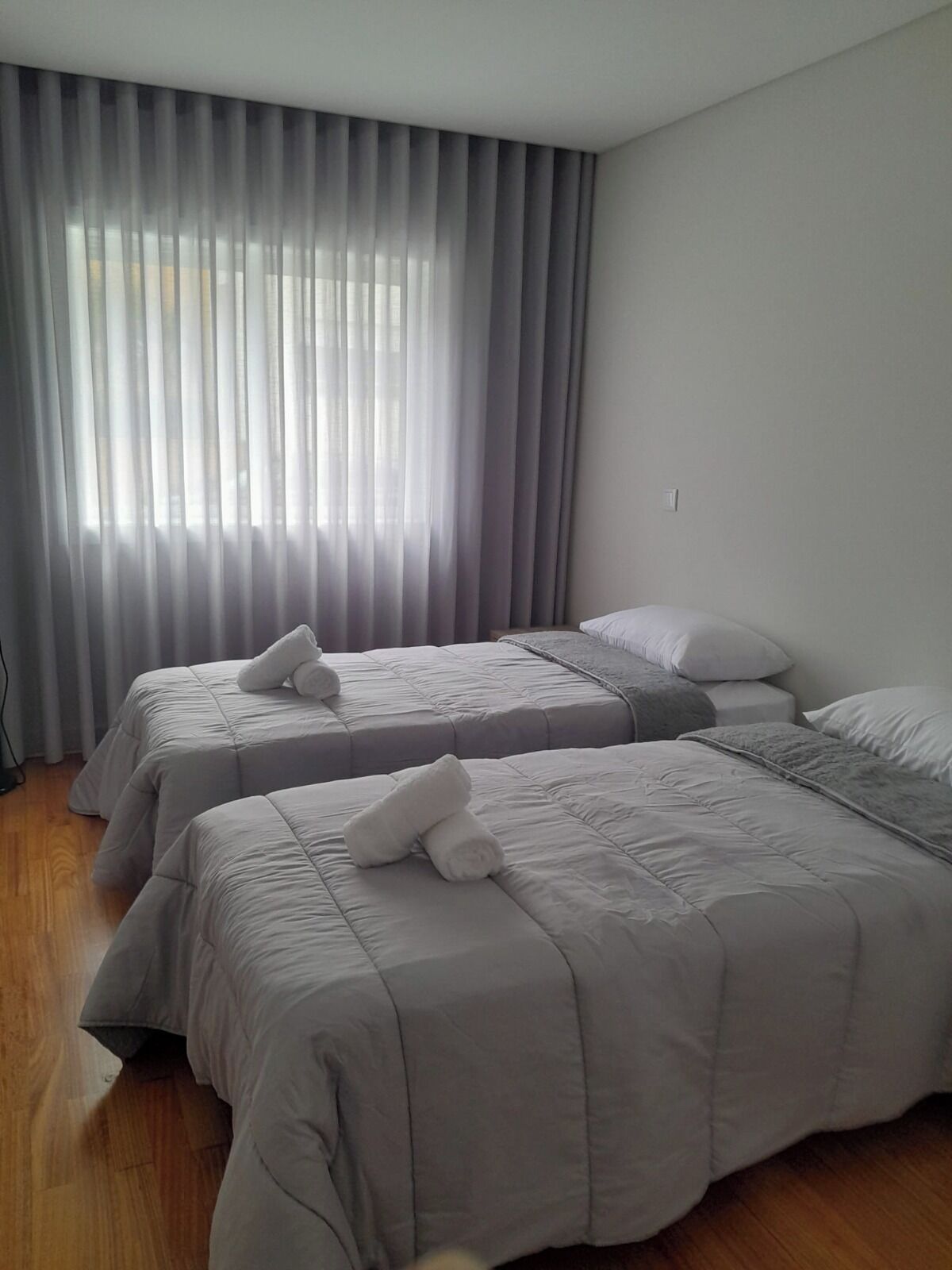 Une chambre d’hôtel avec deux lits, une grande fenêtre avec des rideaux et un plancher en bois.