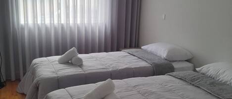 A hotel room with two beds, a large window with curtains, and a wooden floor.