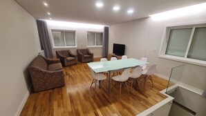 Ein modernes Wohnzimmer mit einem Esstisch mit Glasplatte, weißen Stühlen und braunen Sesseln.