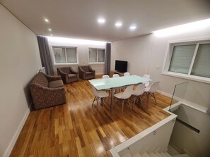 Ein modernes Wohnzimmer mit einem Esstisch mit Glasplatte, weißen Stühlen und braunen Sesseln.