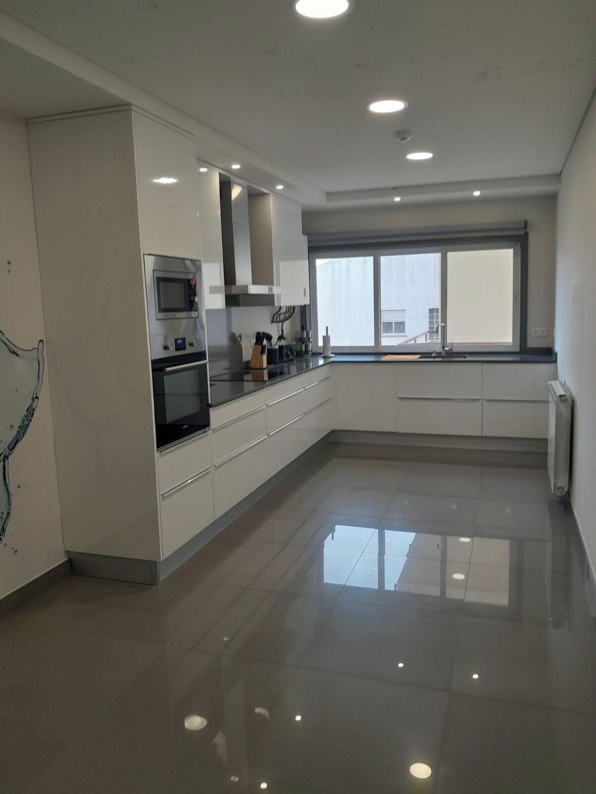 A modern kitchen with stainless steel appliances, white cabinetry, and a large window providing natural light.