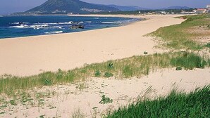 Ein Strand mit einem Berg im Hintergrund, blauem Himmel und einem sandigen Ufer.