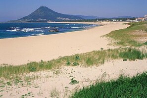 Ein Strand mit einem Berg im Hintergrund, blauem Himmel und einem sandigen Ufer.