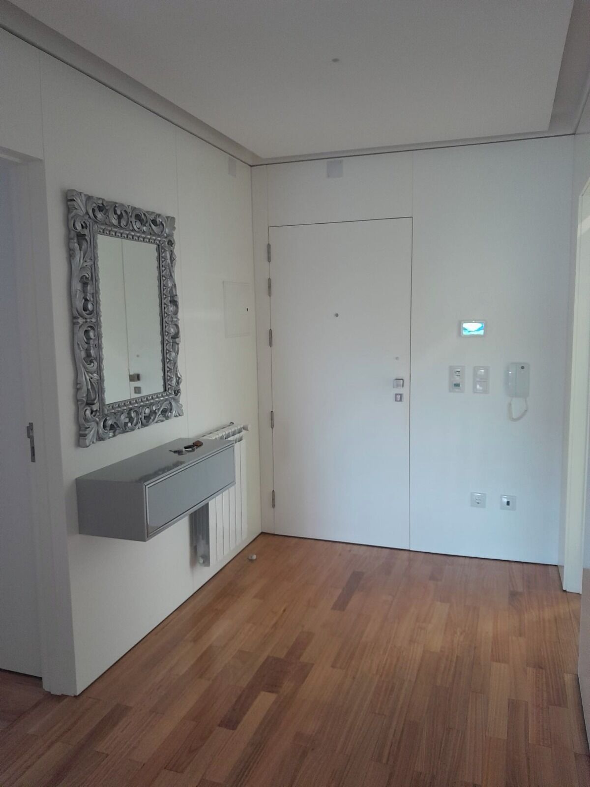 Een kamer met een witte deur, een spiegel met een decoratief omlijsting, een ingebouwde bank en een radiator.