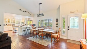 A spacious kitchen with white cabinets, a dining area with wooden chairs and a table, and a large window with a view of greenery. - Summer Place by Avantstay Waterfall Spa + Backyard Atascadero Wine Country (Templeton)