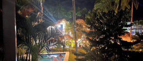 A nighttime view of a resort with a swimming pool, palm trees, and a building with illuminated windows.