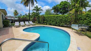 Una piscina de borde curvo, rodeada de sillones de descanso y palmeras.