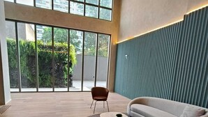 Una sala moderna con un sofá curvo, una mesa de centro redonda y un sillón. Hay un ventanal grande que ofrece vistas a la vegetación exterior.