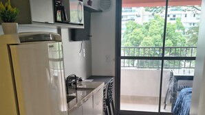 Cocina compacta con refrigerador, lavamanos y zona de comedor con sillas. Un tapete cubre el suelo.