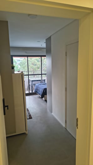A corridor leading to a bedroom with a bed, a window, and a door.