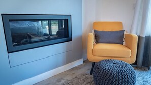 Ein Zimmer mit einem großen Fenster, einem gelben Sessel und einem gestrickten Hocker.