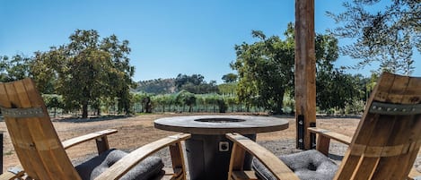 A circular outdoor seating area with a fire pit, surrounded by wooden chairs with cushioned seats.
