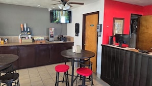 Interior de un restaurante con barra, ventilador de techo, televisión montada en la pared y una pared de acento roja.