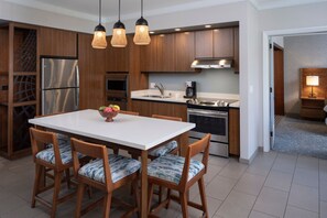 Eine moderne Küche mit Holzausstattung, einem Edelstahlkühlschrank, einem Einbauofen und einem Essbereich mit weißem Tisch und gemusterten Stühlen.