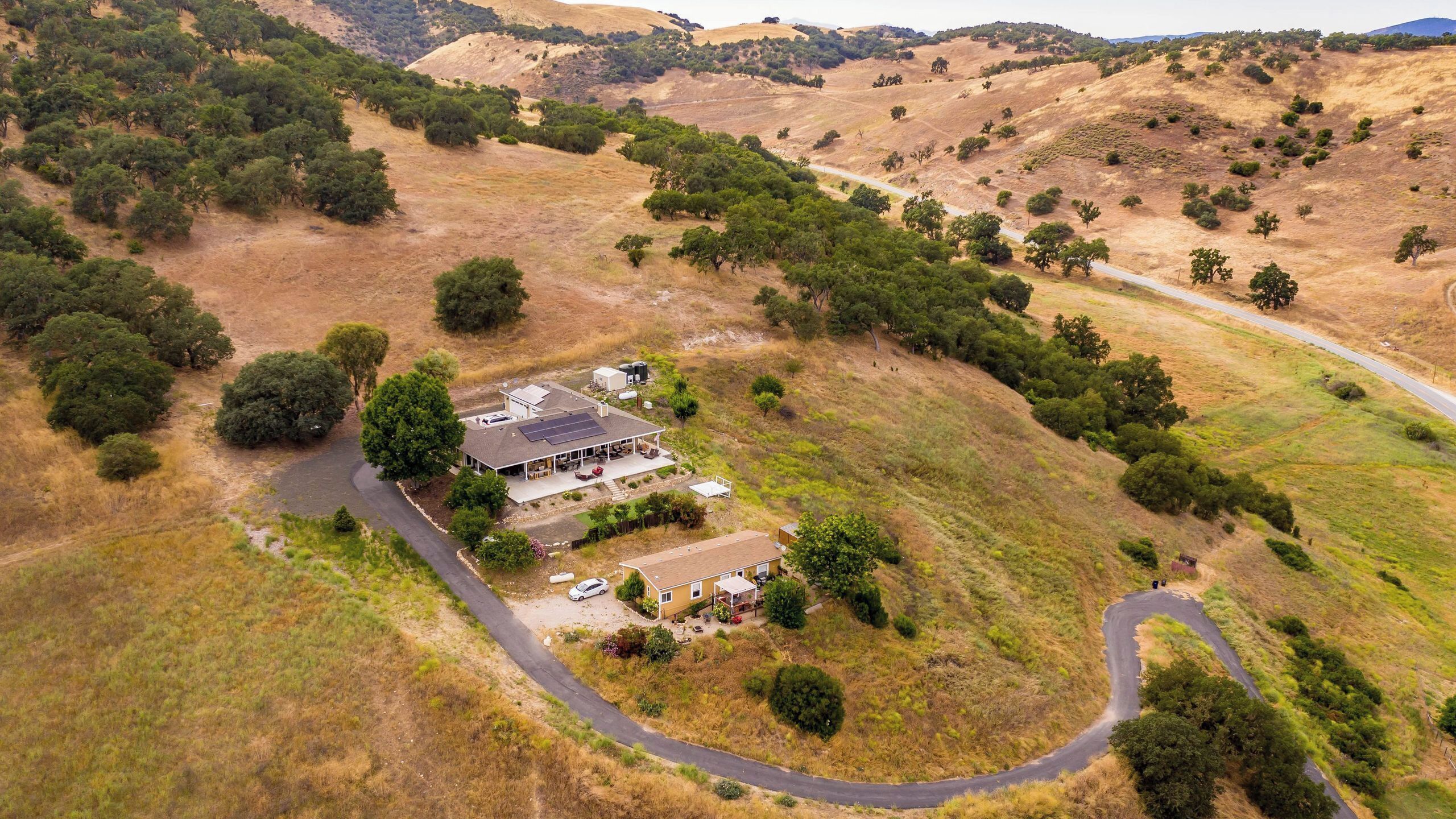 A house with a large patio area, surrounded by a hilly landscape with sparse vegetation.