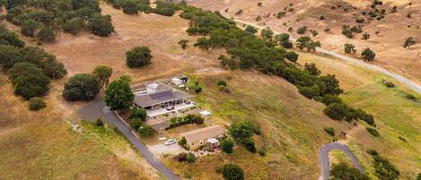 A house with a large patio area, surrounded by a hilly landscape with sparse vegetation.