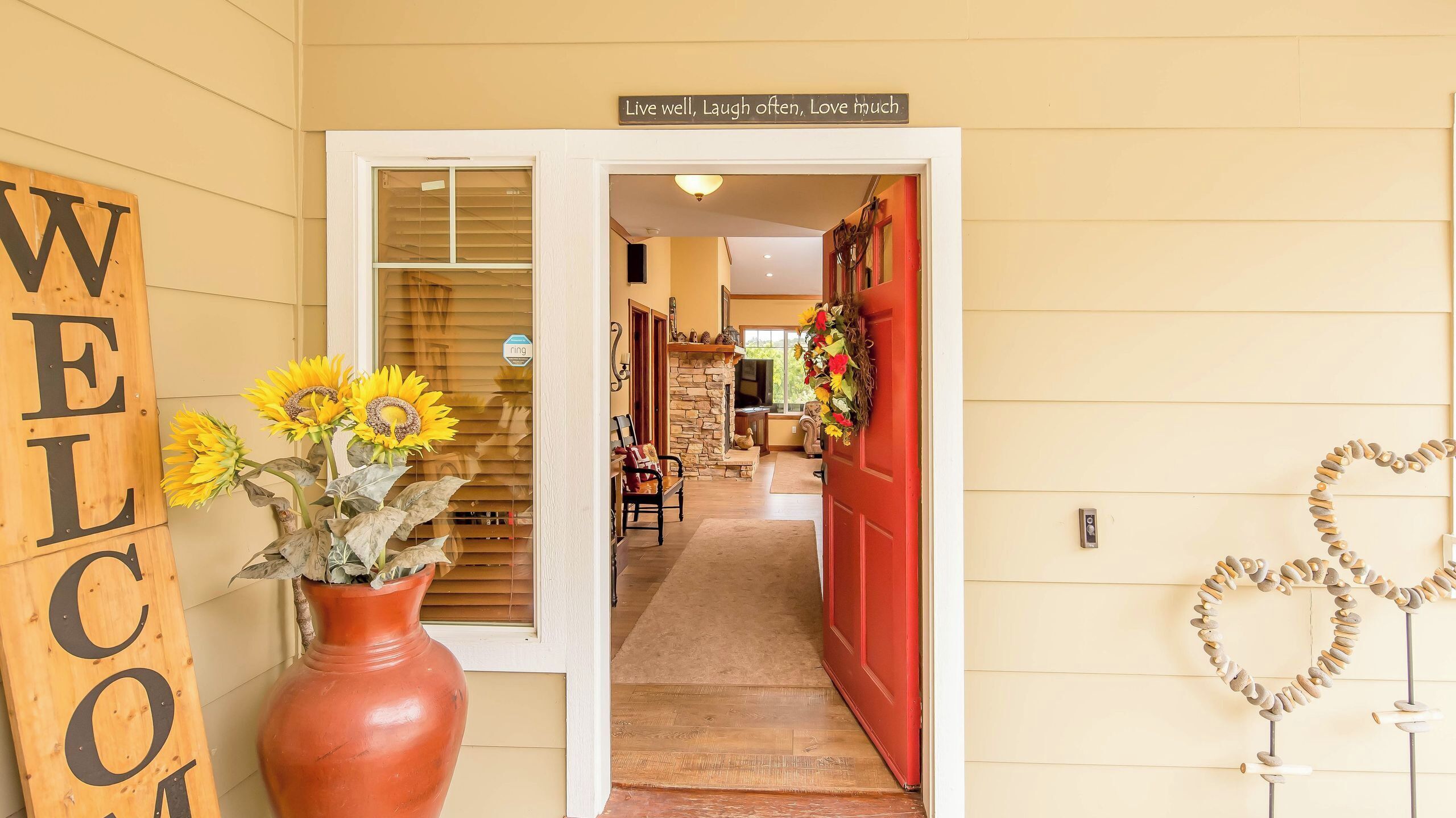 A hallway with a welcome sign, a vase of sunflowers, a red door, and a heart-shaped decoration.