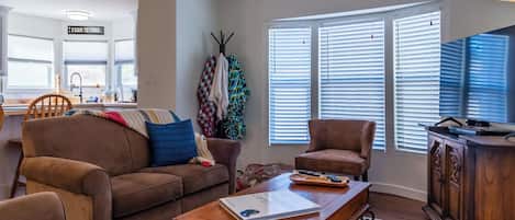Una sala de estar con un sofá marrón, una mesa de centro de madera y un televisor sobre un mueble de madera.
