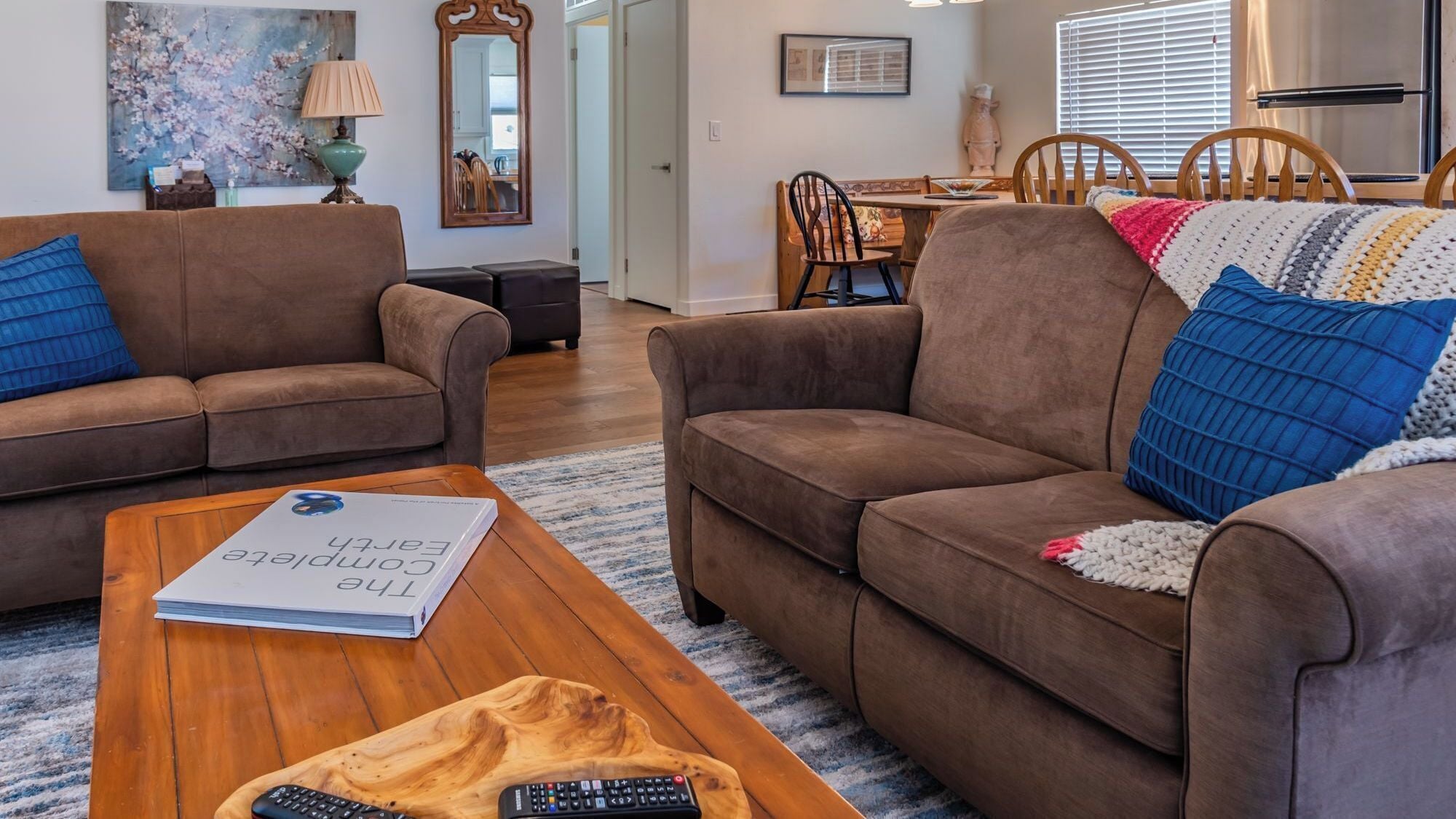 A living room with two brown sofas, a coffee table, and a dining area with wooden chairs.